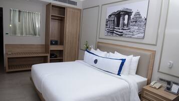A hotel room with a large bed, a wardrobe, a bedside table with a phone, and a framed picture on the wall.