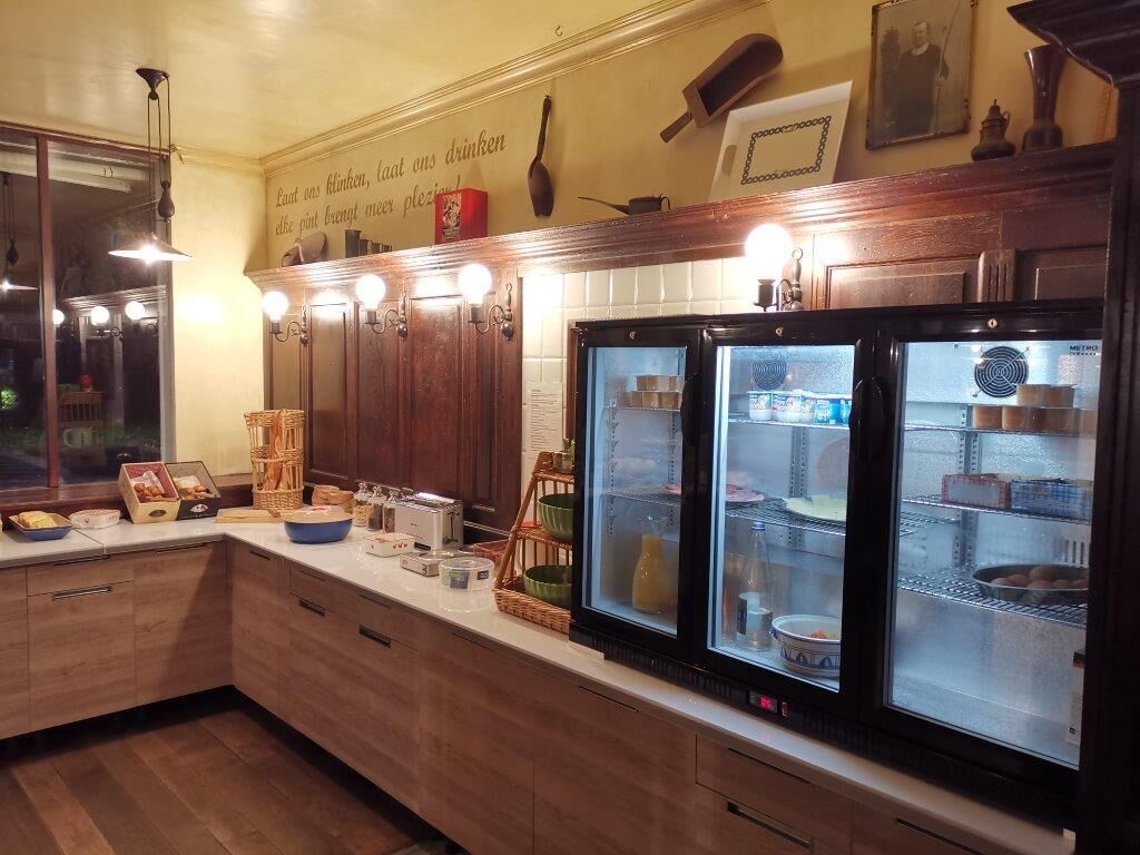 Une cuisine avec des meubles de rangement en bois, un plan de travail sur lequel se trouvent divers objets, et deux réfrigérateurs à portes vitrées.