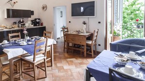 Un coin repas avec une table et des chaises en bois, un téléviseur fixé au mur et un balcon offrant une vue sur la verdure.