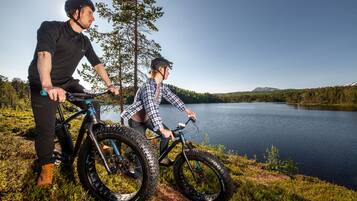 Dos personas en bicicleta junto a un lago, con un bosque al fondo.