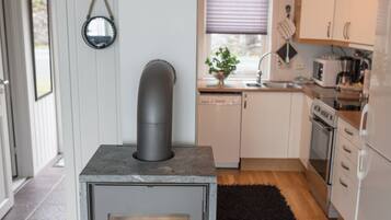 Une cuisine de taille réduite, dotée d’un poêle à bois, de meubles blancs et d’un tapis noir.
