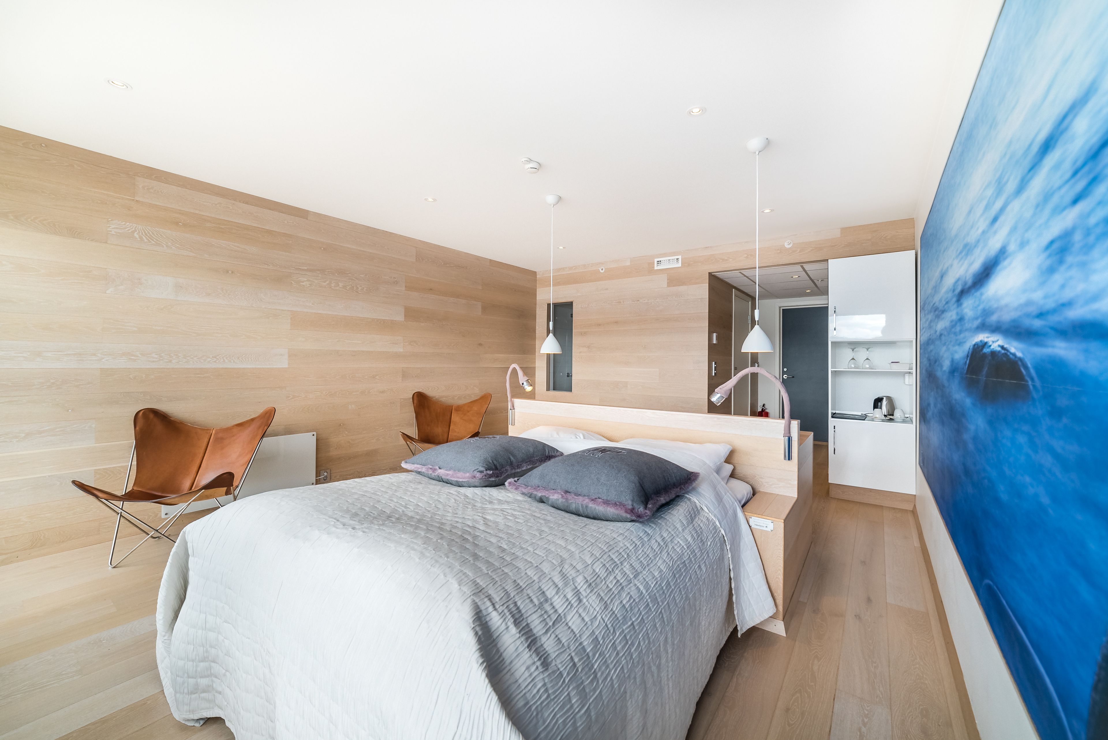 A modern bedroom with a large bed, a chair, and a kitchenette area.