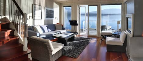 A spacious living area with a wooden staircase, a sofa, a coffee table, and a television.