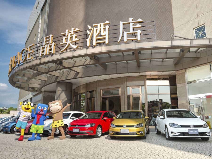 Entrada de un hotel con fachada curva, un letrero con caracteres chinos y varios coches estacionados al frente.