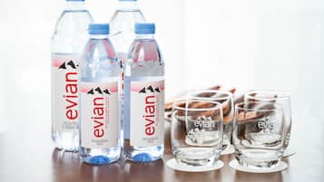 Three Evian water bottles and four glasses on a wooden surface.