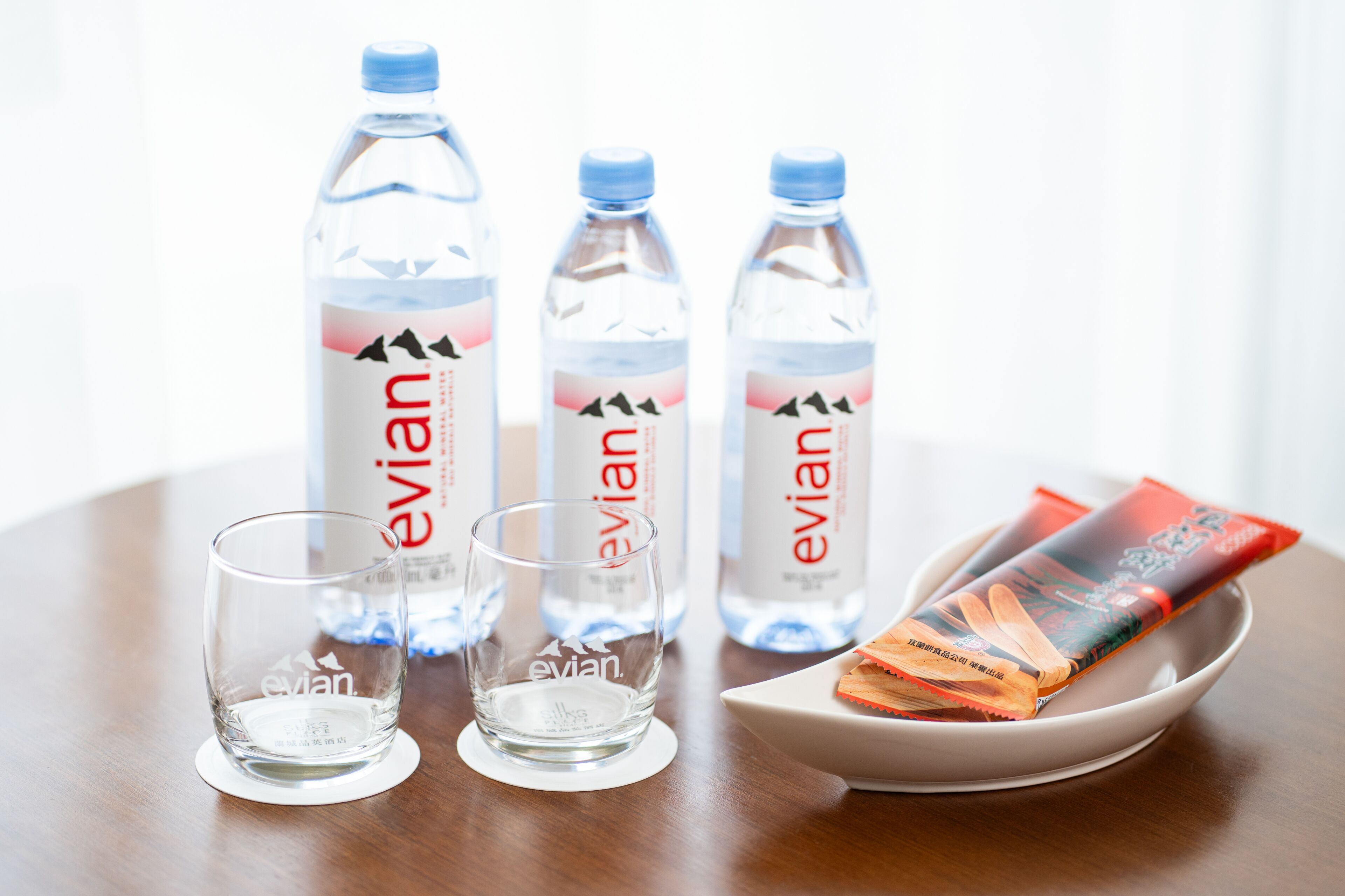 Three Evian water bottles, two glasses, and a snack package on a table.