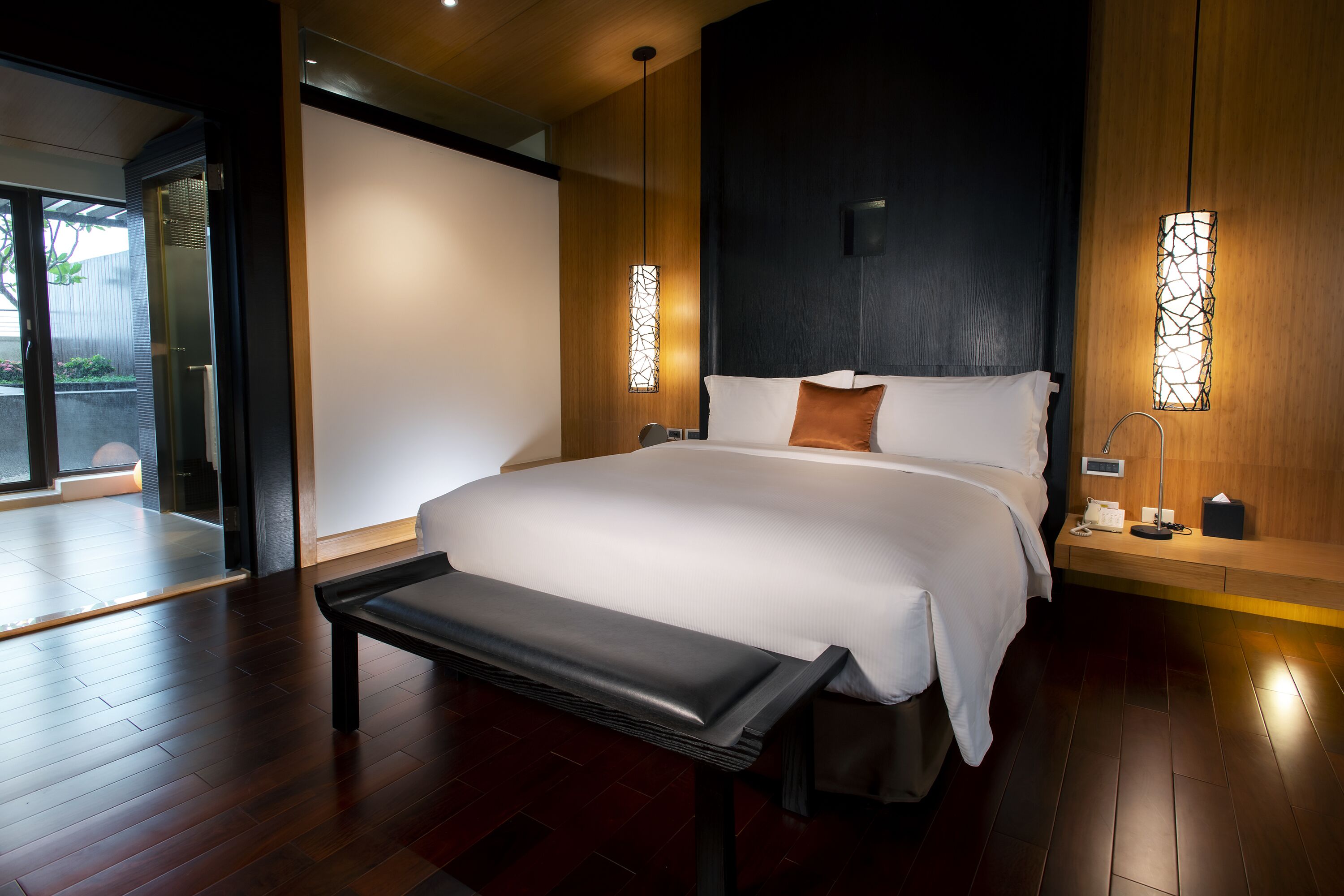 A modern hotel room with a large bed, a bench, and two wall-mounted lamps.