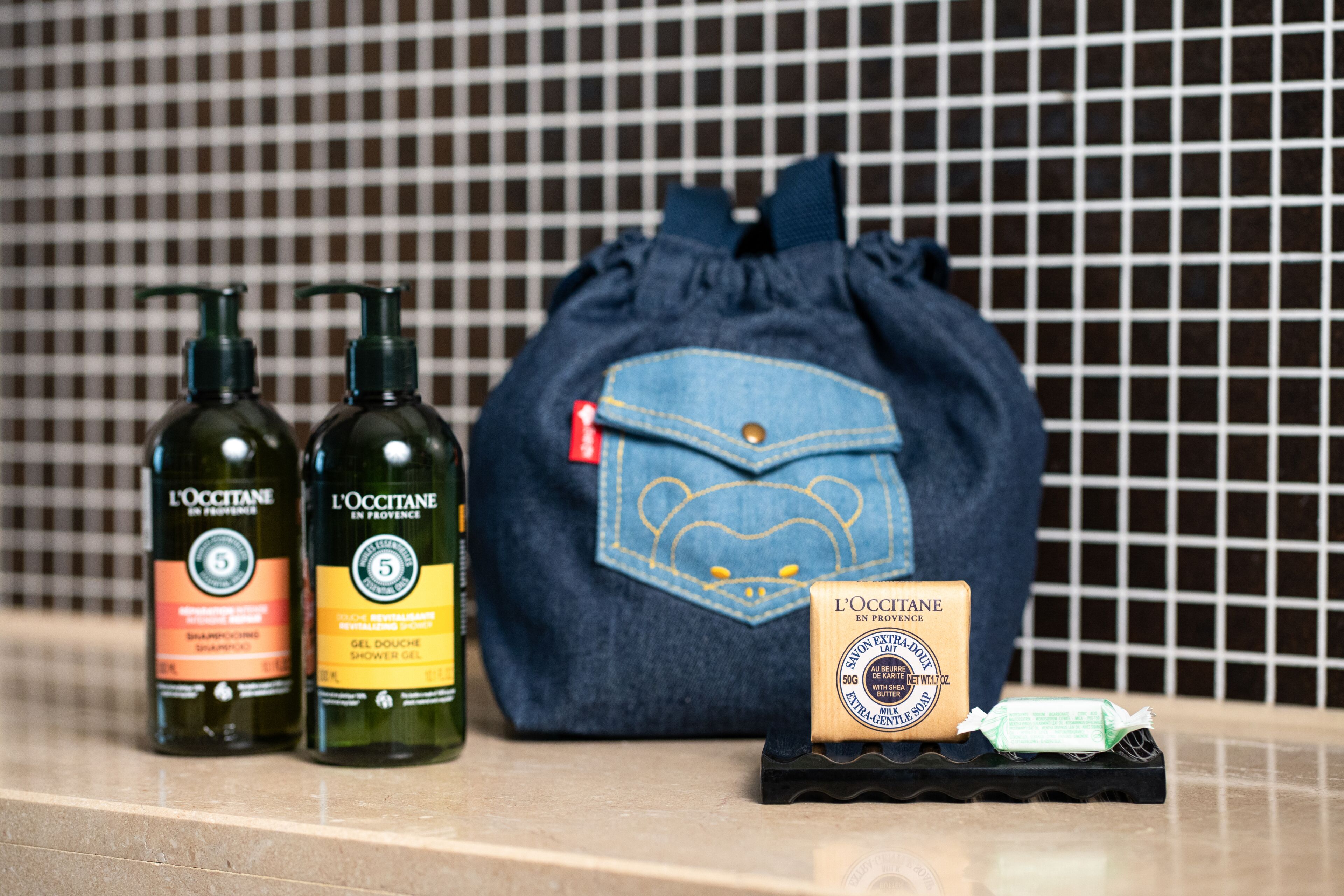 Toiletries including shampoo, shower gel, and soap, arranged on a countertop with a tiled backsplash.