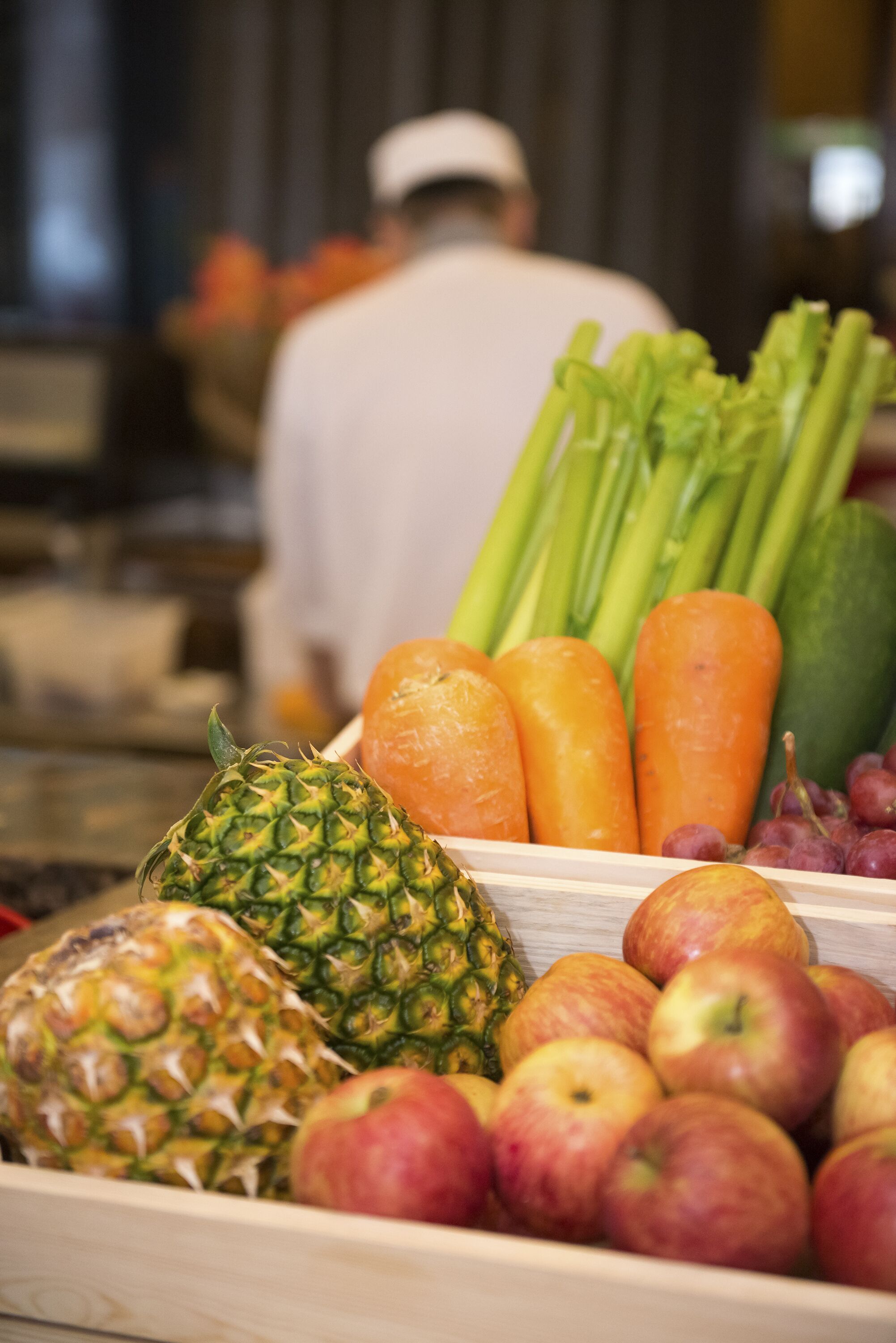 A wooden fruit and vegetable display with apples, pineapple, celery, carrots, and grapes.