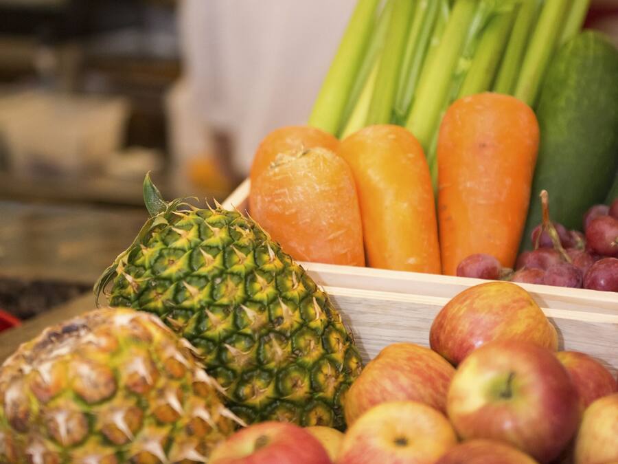 A wooden fruit and vegetable display with apples, pineapple, celery, carrots, and grapes.