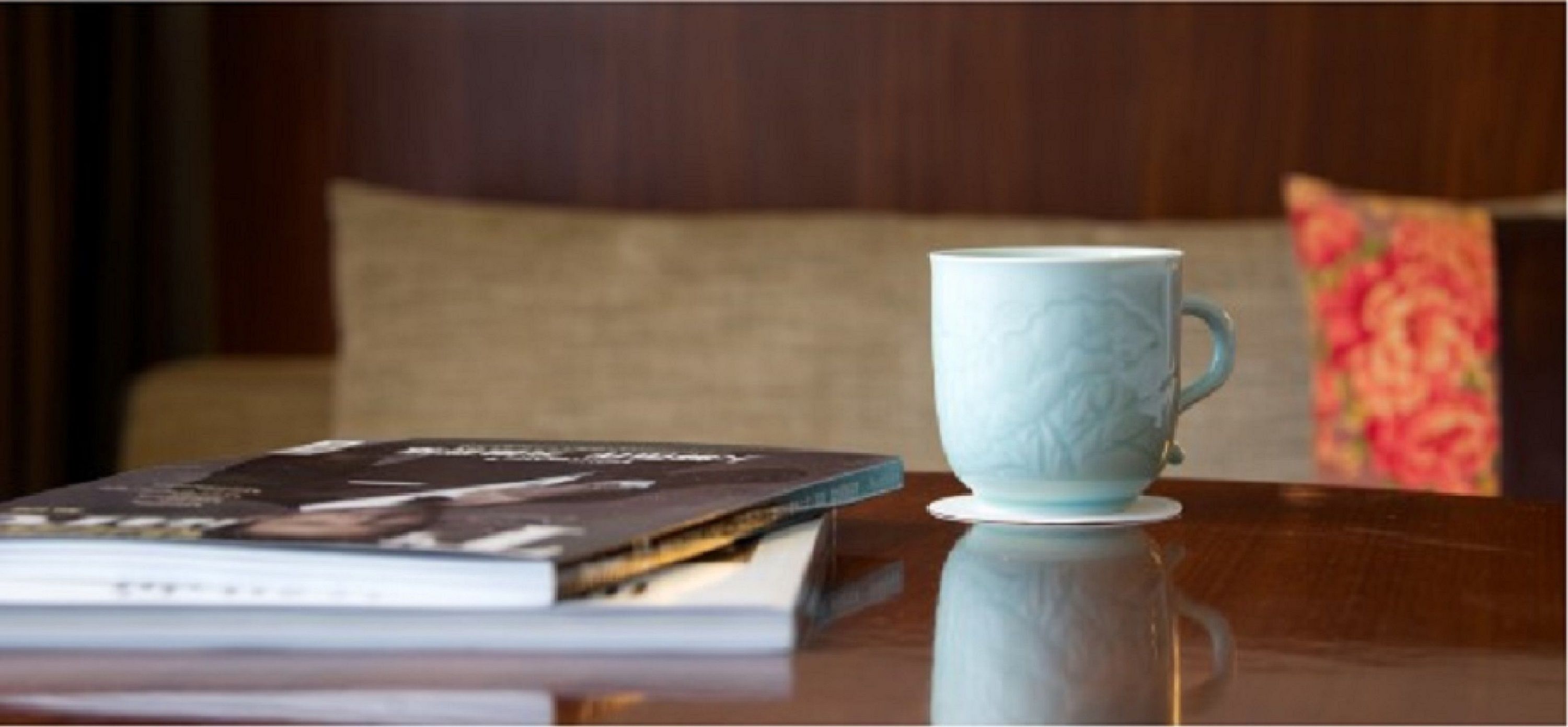 Un libro y una taza de cerámica sobre una superficie reflectante.