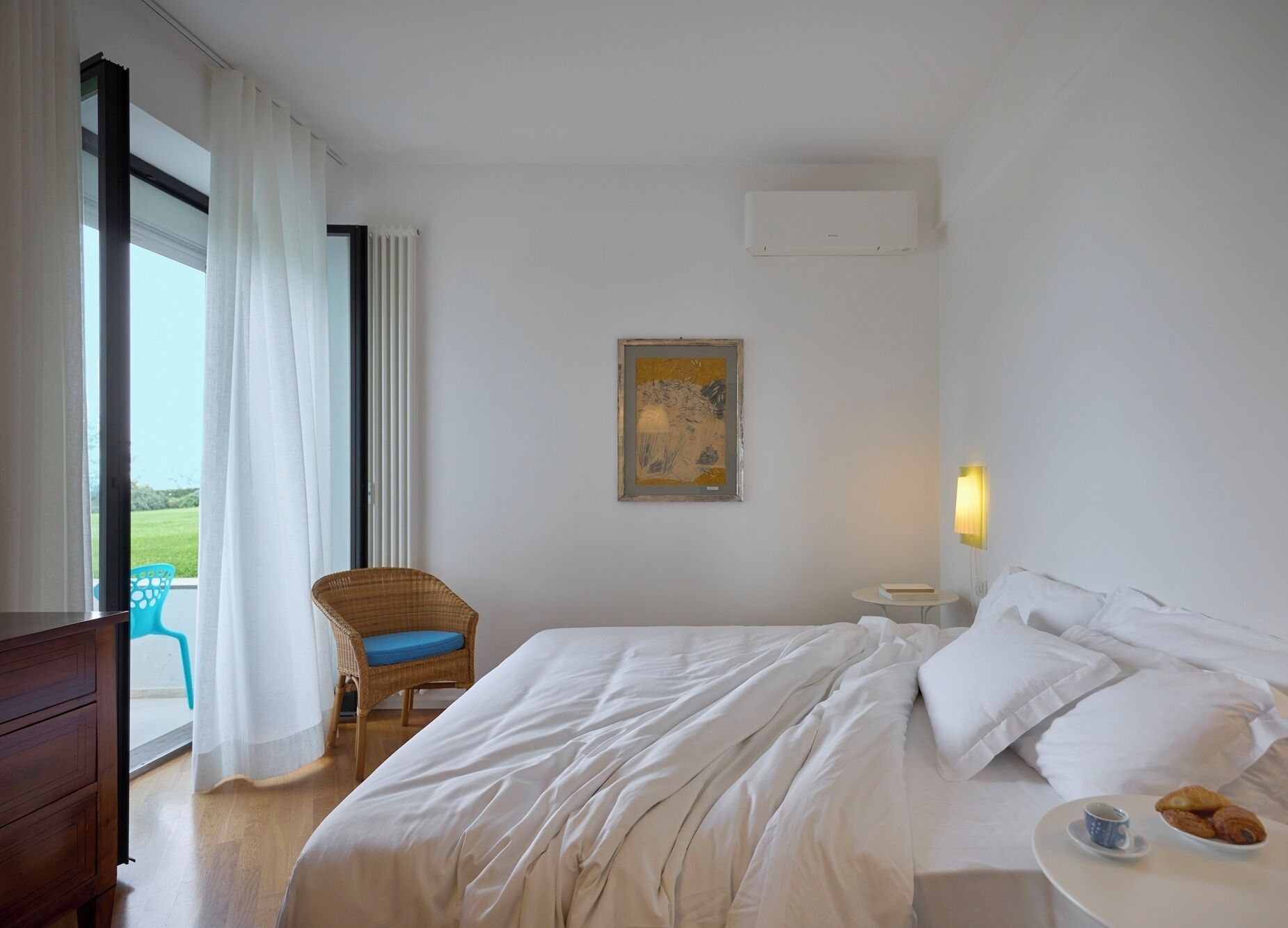 Une chambre d’hôtel avec un lit, une chaise, un tableau, une table de chevet avec une lampe et une vue sur l’extérieur.