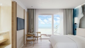 Habitación de hotel con cama, escritorio con sillas, televisión y vista a la playa.