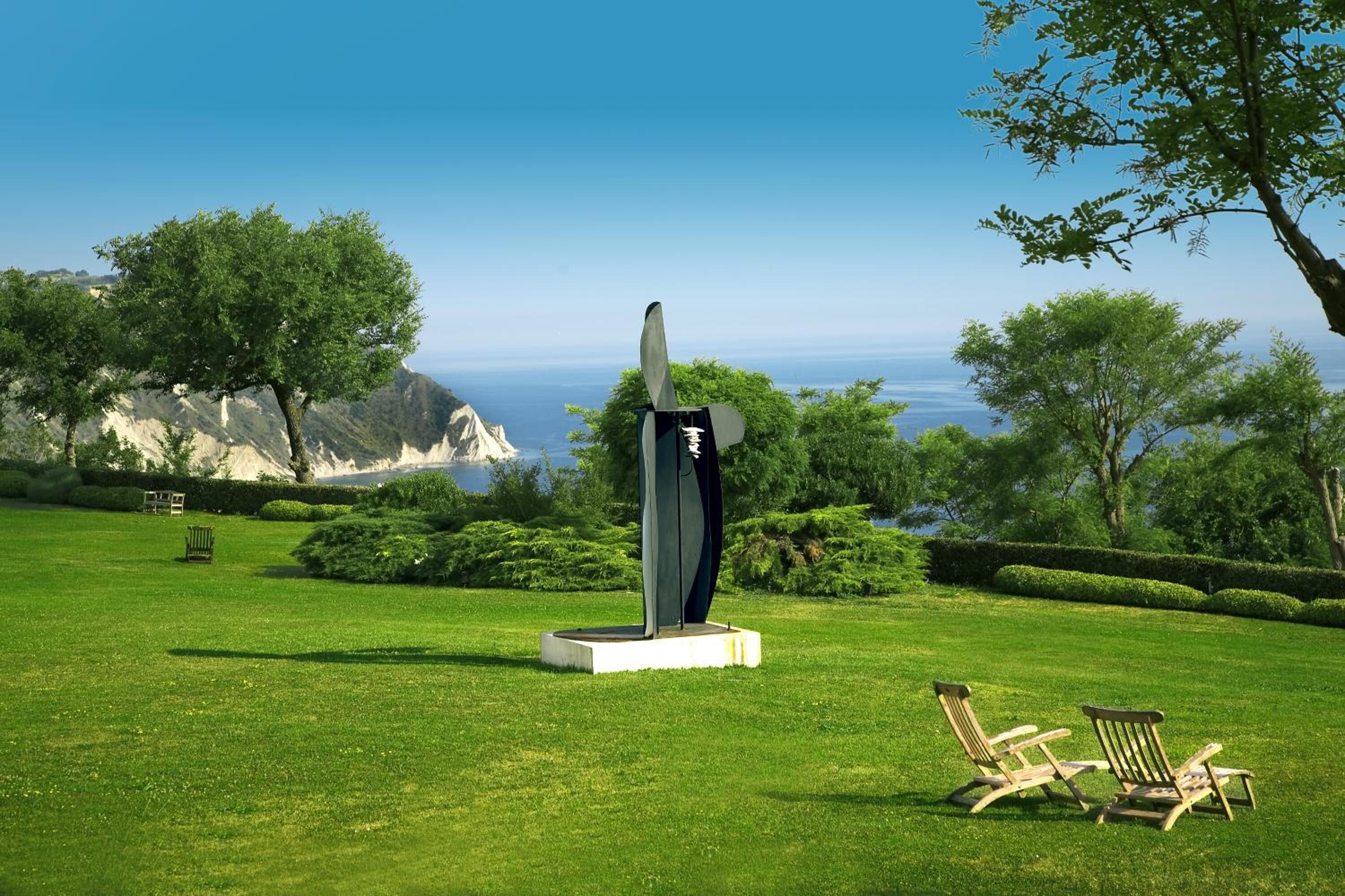 A sculpture in a grassy area with a view of the ocean and mountains in the background.