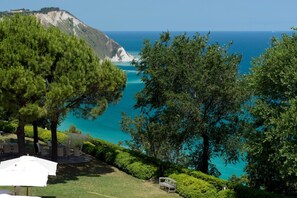 A coastal view with a grassy area, trees, and a white umbrella.
