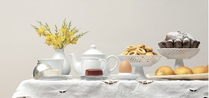 Una mesa dispuesta con tetera, un jarrón con flores amarillas, un tazón de galletas, un muffin y una cesta de pan.