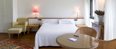 A hotel room with a bed, two bedside lamps, a chair, a small table, a nightstand, and a decorative vase.