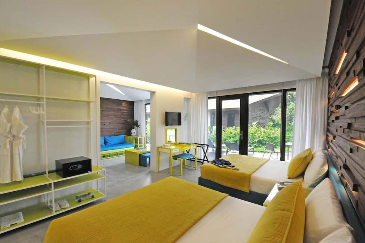 Habitación de hotel moderna con dos camas, un escritorio, un televisor y un balcón con vistas a zonas verdes.