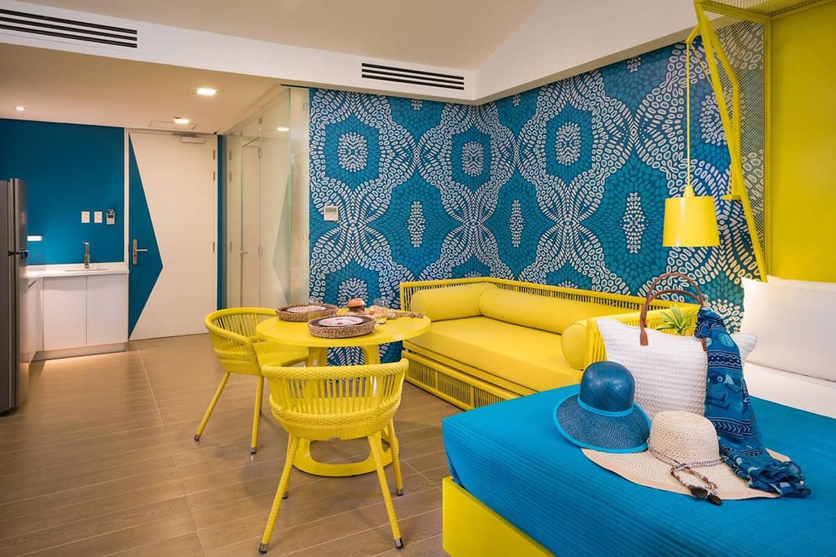 Una habitación moderna con un sofá amarillo, una mesa redonda con sillas y una pared con estampado.