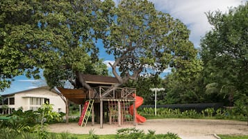 Un parque infantil con tobogán y estructura para escalar, rodeado de árboles y vegetación.