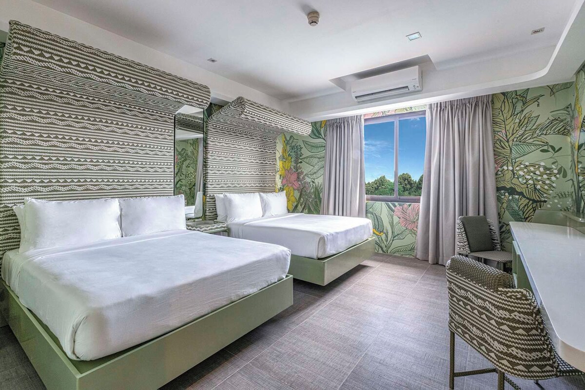 A hotel room with two beds, a desk, and a view of the outdoors.