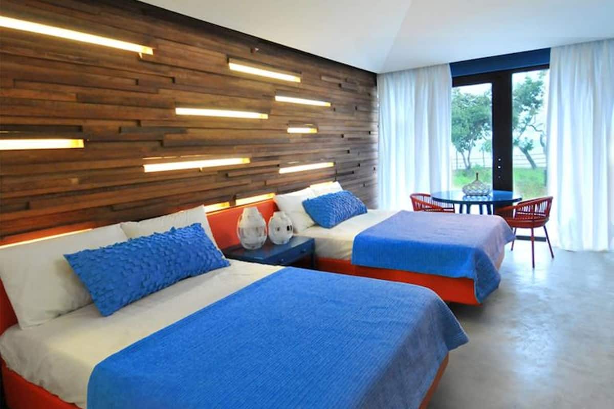 Una habitación de hotel moderna con dos camas, un cabecero de madera y vistas al exterior.