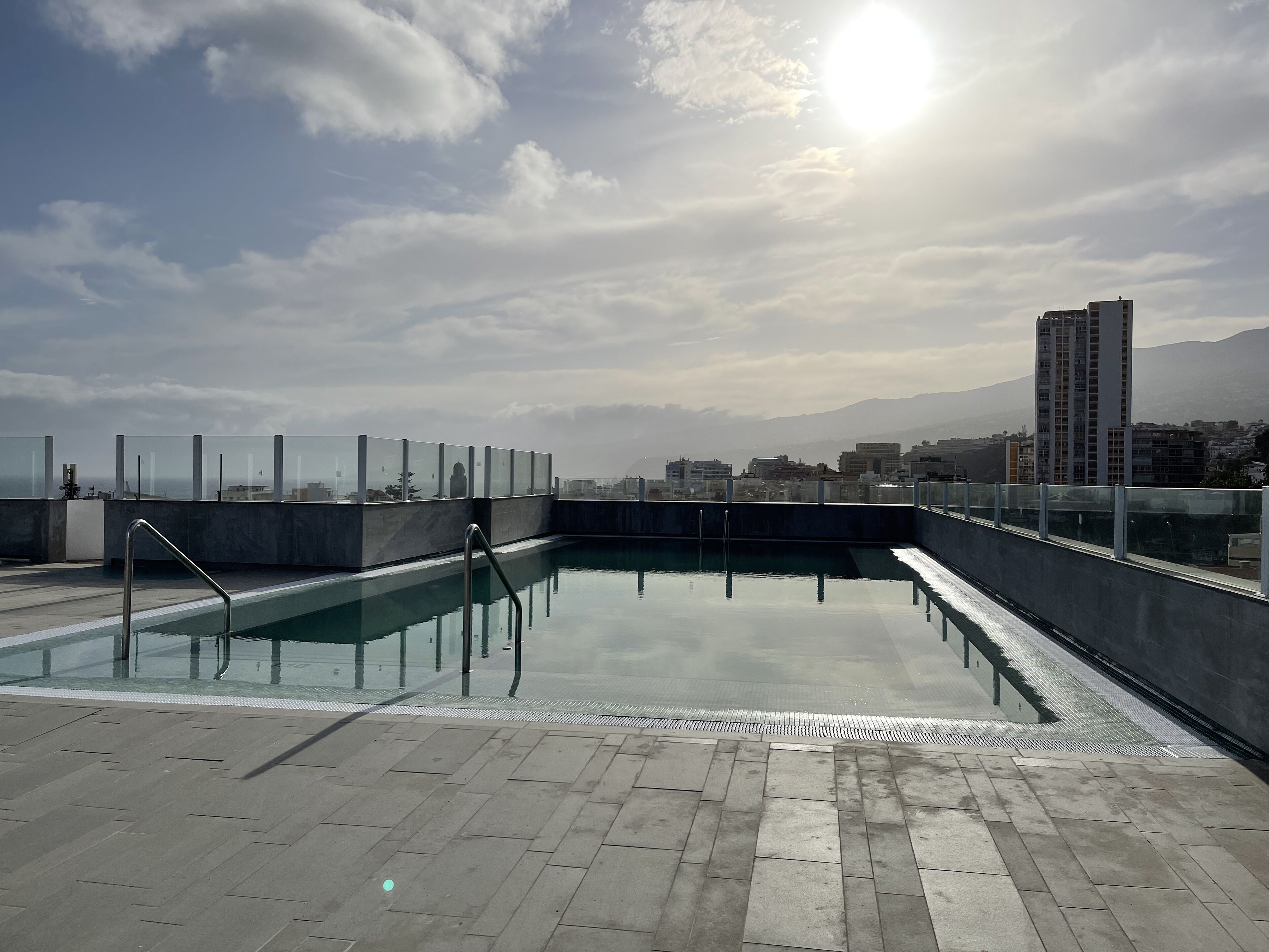 A rooftop pool with clear glass barriers, a metal ladder, and a tiled floor.