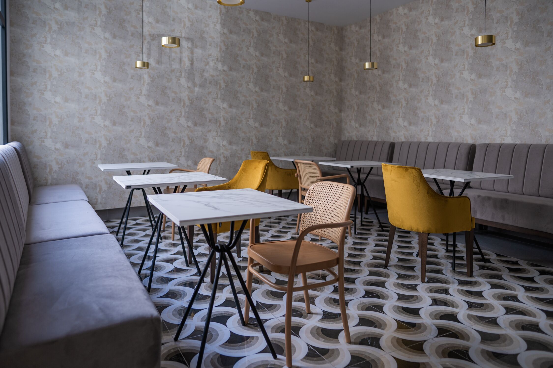 Interior de un restaurante moderno con suelo estampado, asientos grises y sillas amarillas.