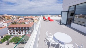 A rooftop terrace with a table and chairs, red lounge chairs, and a view of the city and sea. - Hotel AF Valle Orotava (Puerto de la Cruz)