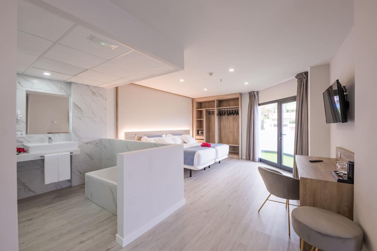 A modern hotel room with a bathroom, a sitting area, a bed, a TV, and a balcony.