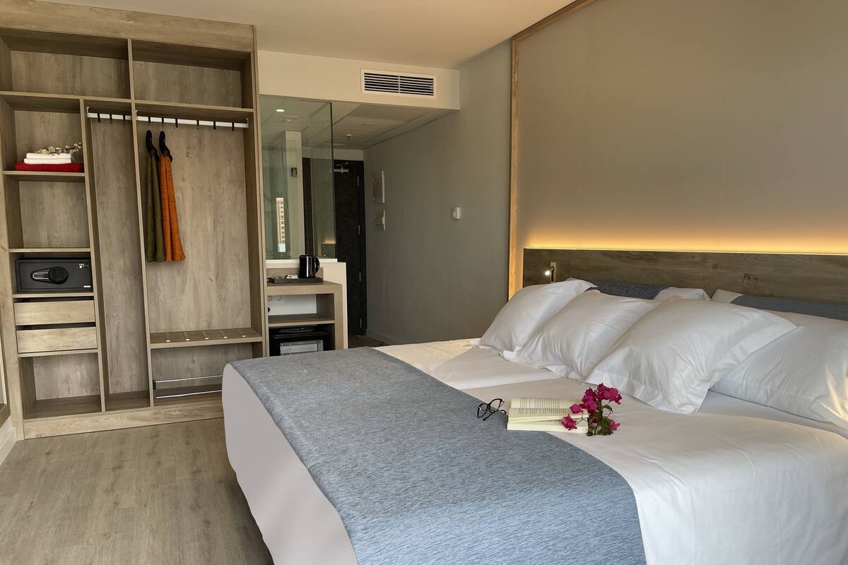 A modern hotel room with a large bed, a walk-in closet, a bathroom, and a small seating area.