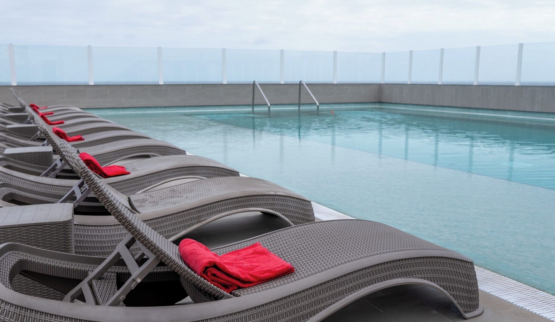 Un área junto a la piscina con filas de sillones de mimbre, cada uno con una toalla roja.