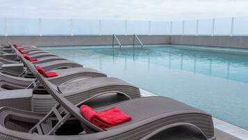 Un área junto a la piscina con filas de sillones de mimbre, cada uno con una toalla roja.