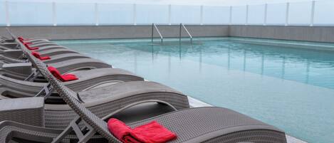 Un área junto a la piscina con filas de sillones de mimbre, cada uno con una toalla roja.