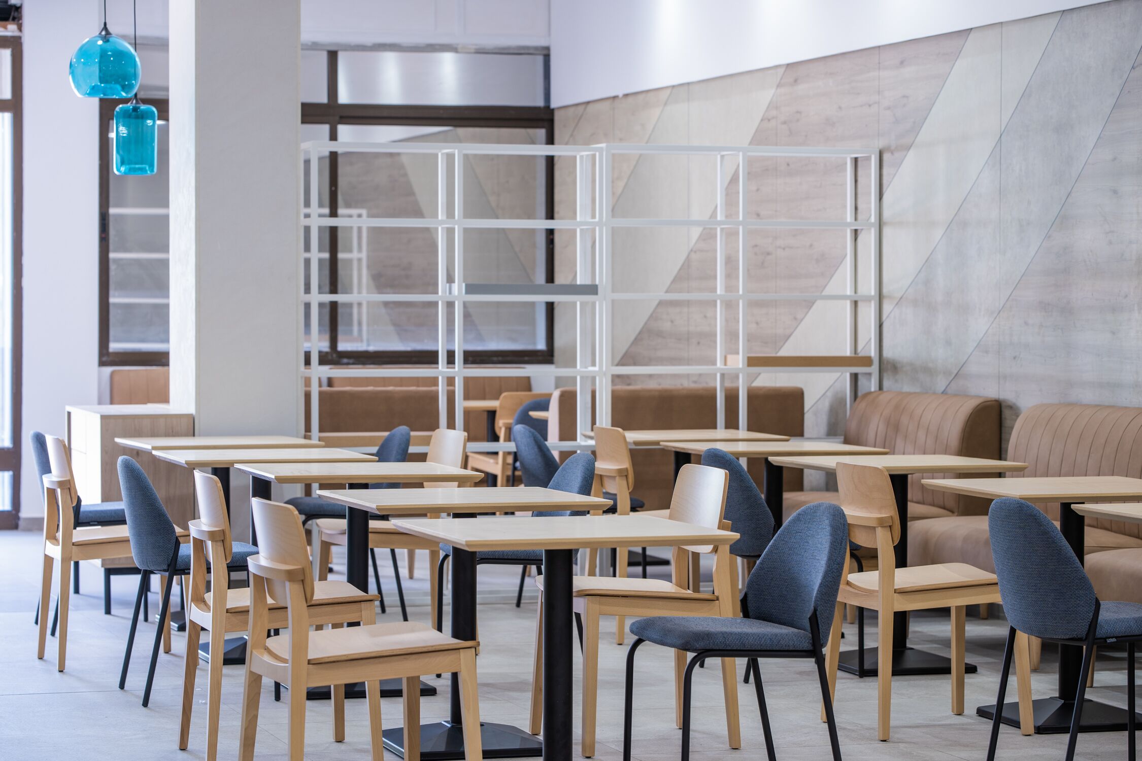 A modern restaurant interior with wooden tables and chairs, a geometric wall design, and hanging blue pendant lights.