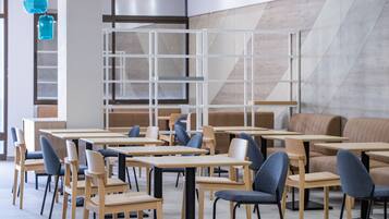 Un interno ristorante moderno con tavoli e sedie in legno, un design geometrico per le pareti e lampade pendenti blu.