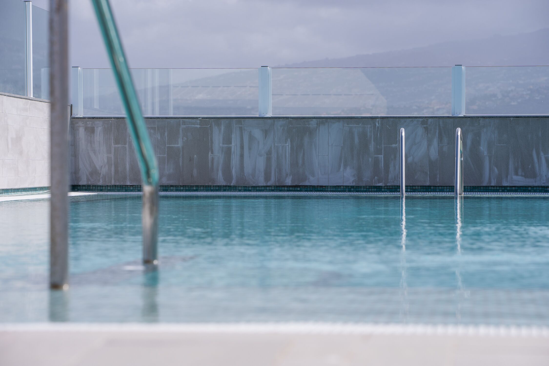 A swimming pool with clear water, metal railings, and a view of mountains in the background.