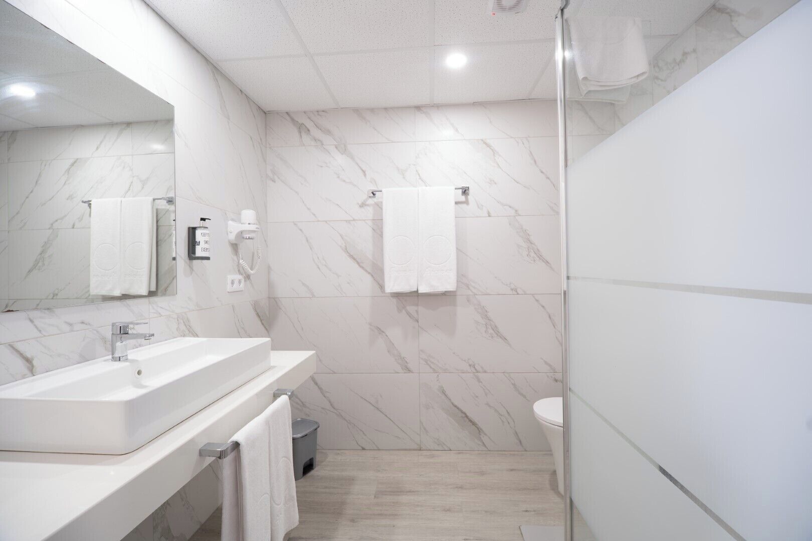 A modern bathroom with a marble backsplash, a large mirror, a sink, and a shower area.