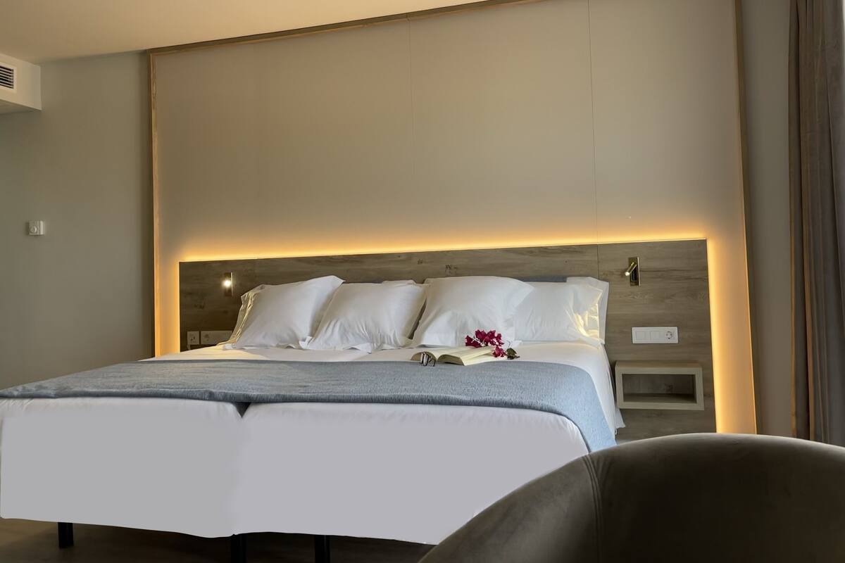 A modern hotel room with a large bed, a bedside table, and a headboard with integrated lighting.