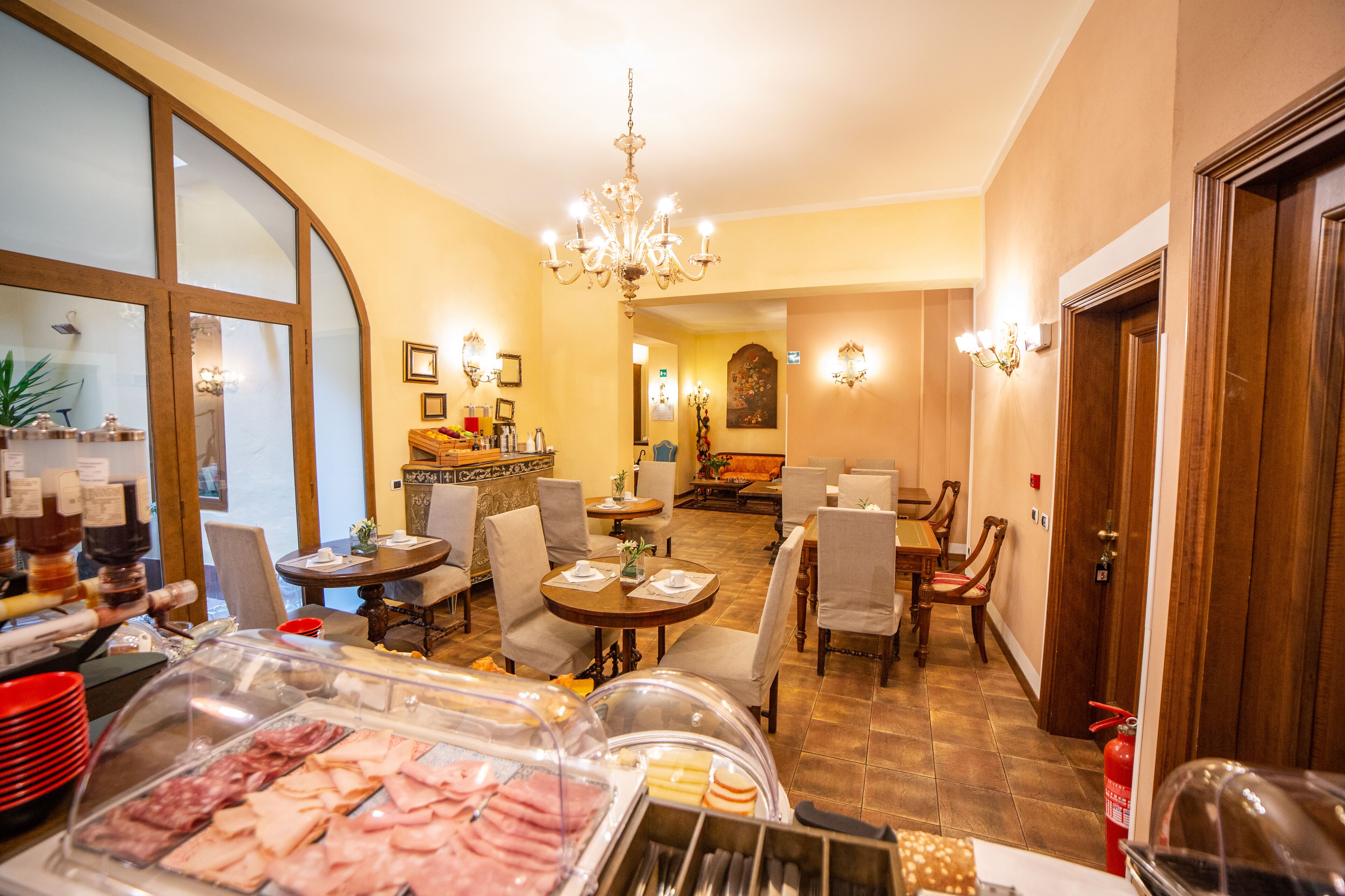 A hotel dining area with a buffet, seating arrangements, and a chandelier.