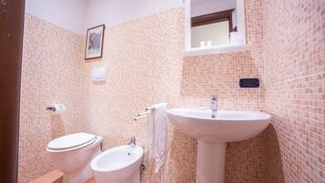 Un baño con inodoro, bidé, lavabo y paredes con azulejos.