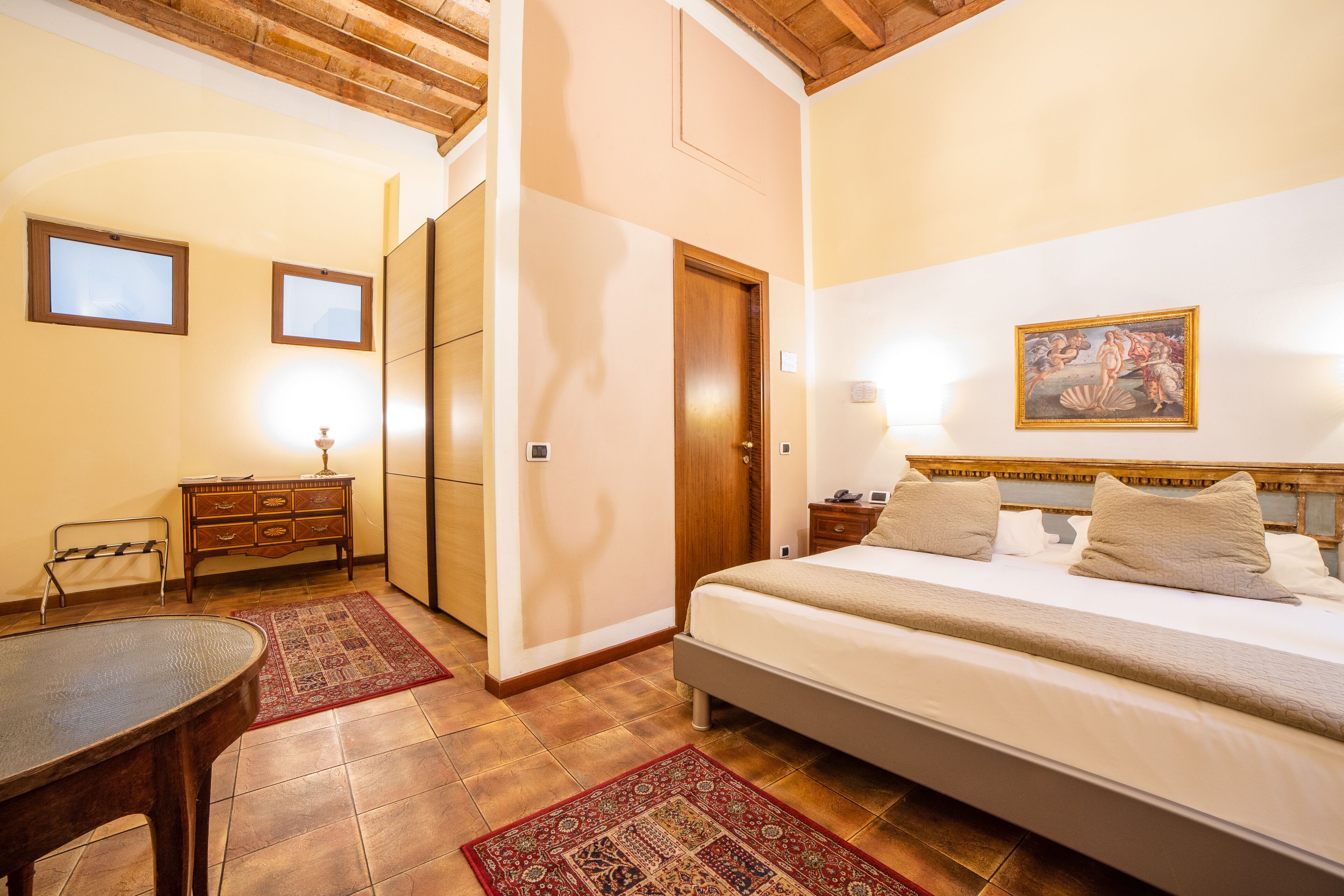 A bedroom with a bed, bedside tables, a wooden wardrobe, a desk, and a chair.