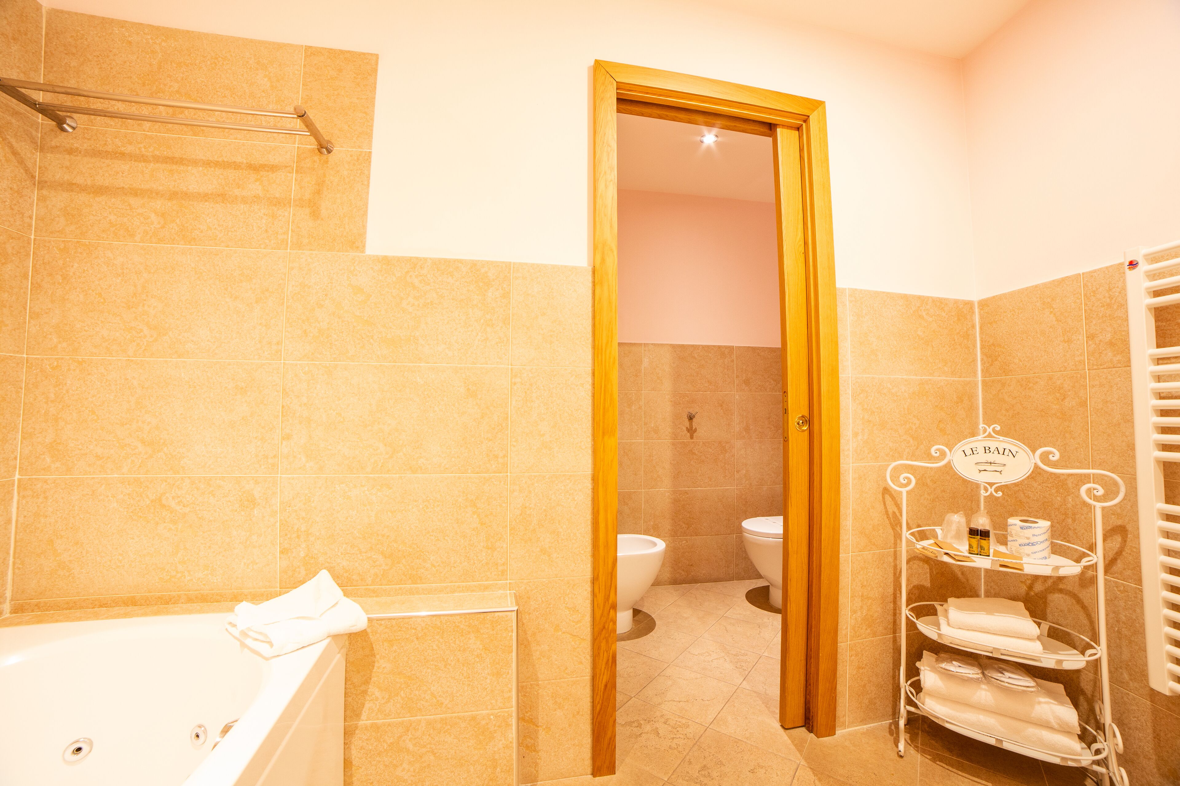 A bathroom with a bathtub, two toilets, and a towel rack with a sign.
