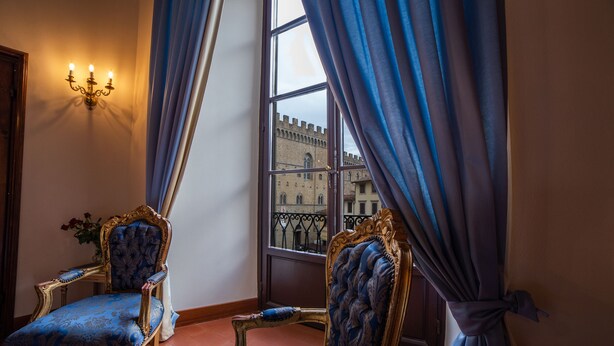 A room with two ornate chairs, a wall-mounted light fixture, and a window with curtains. - B&B Galileo 2000 (Florence)