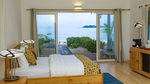Une chambre avec un lit, des lampes de chevet, une armoire en bois et une vue sur la plage grâce à de grandes portes-fenêtres coulissantes.