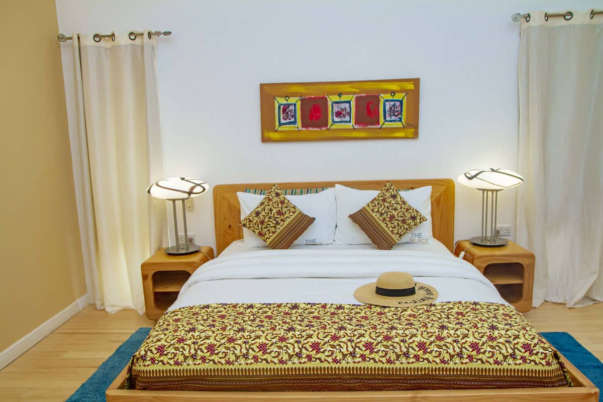 Ein ordentlich eingerichtetes Schlafzimmer mit einem Bett, zwei Nachttischen, einem Wandbild und einem Hut auf dem Bett.