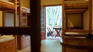 A wooden bunk bed room with a small table and chairs, a window with a view of trees, and a door leading outside. - Escambo Hostel (Sao Paulo)