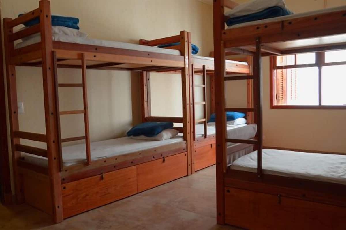 Une pièce avec trois lits superposés en bois, chacun étant équipé d’un matelas et d’oreillers. Il y a une fenêtre sur le côté droit de la pièce.