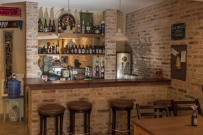 A bar area with a brick wall, shelves with bottles, a refrigerator, and stools. - Escambo Hostel (Sao Paulo)