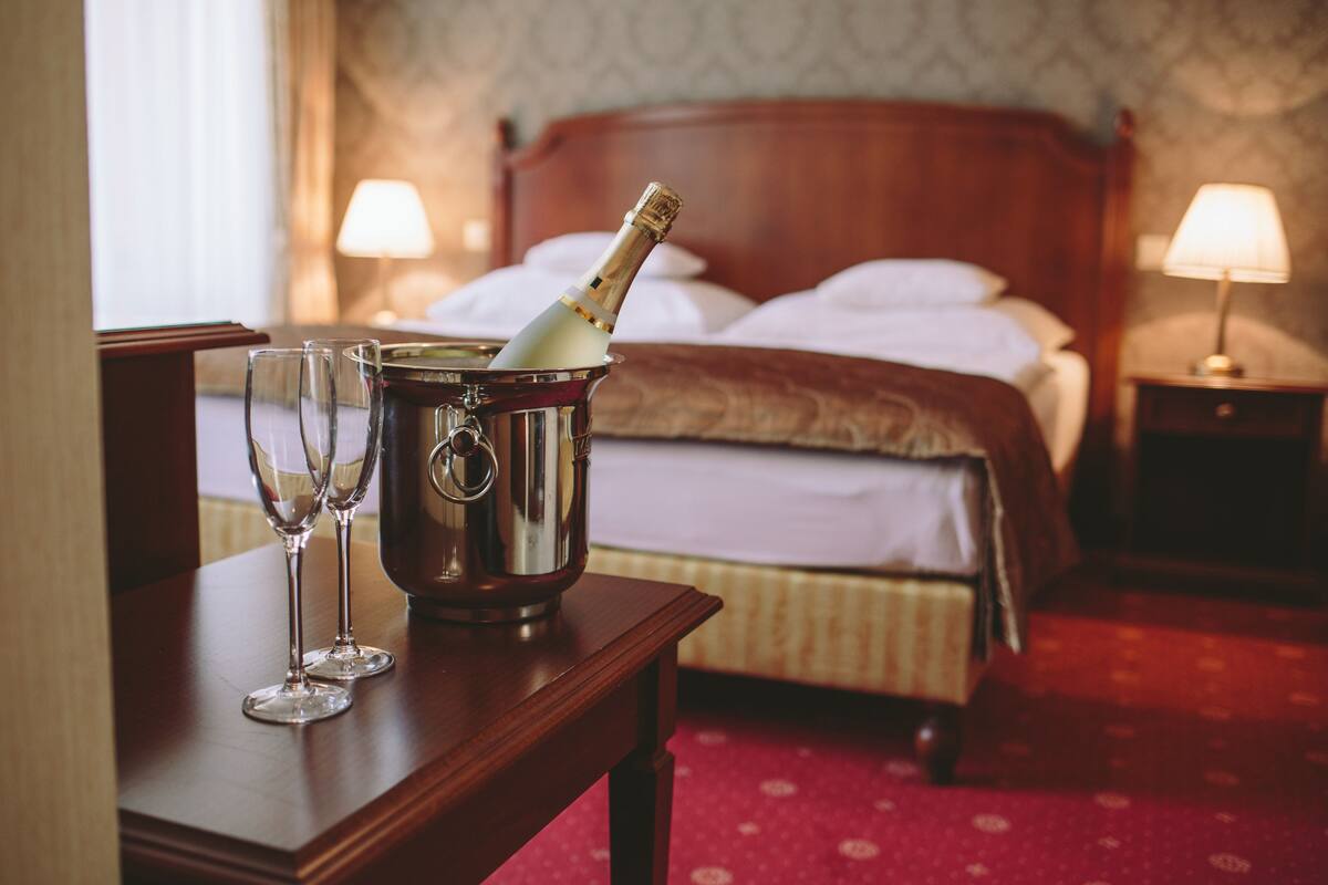 A hotel room with a wooden bed, two bedside lamps, a red carpet, and a bottle of champagne in a metal bucket.